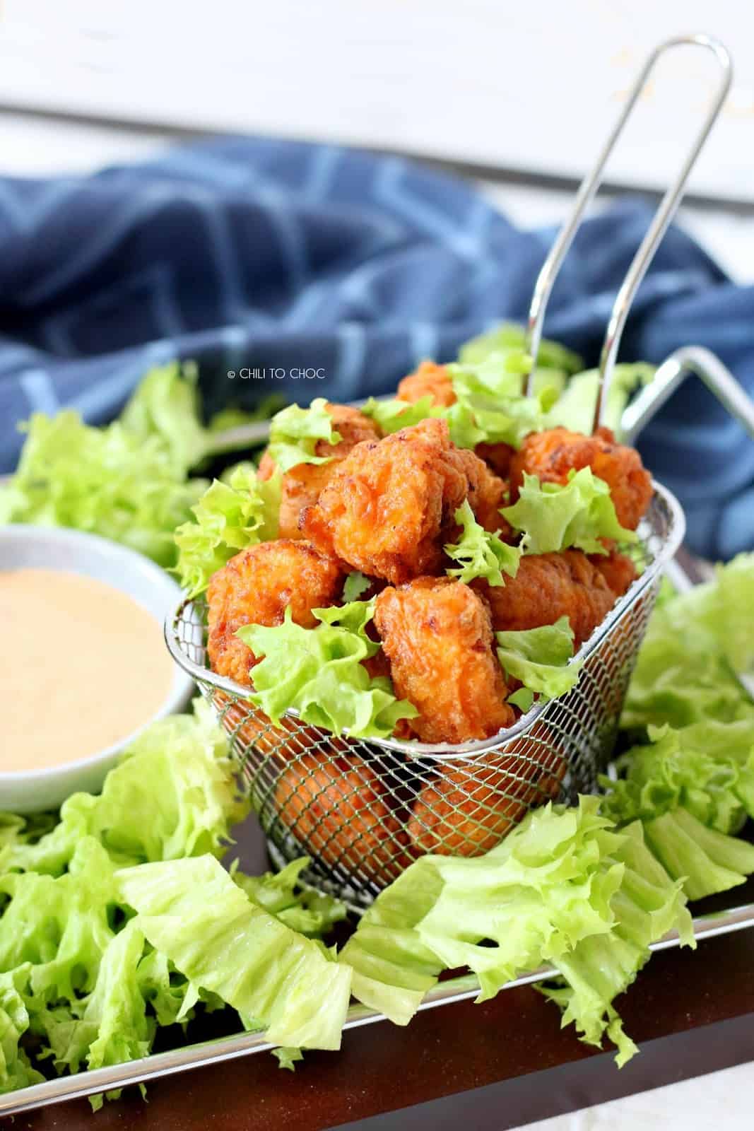 Popcorn chicken in a fries basket on a platter of shredded lettuce with a dip on the side.