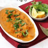 Authentic Chicken Tikka Masala in a white serving dish with coriander and lemon wedges on the side