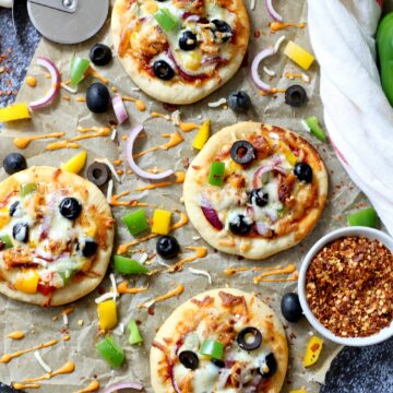 Peri Peri Mini Pizzas on a parchment paper with seasoning on the side.