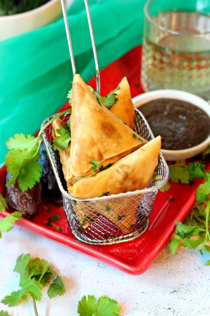 samosas in a fryer basket with chutney at the back