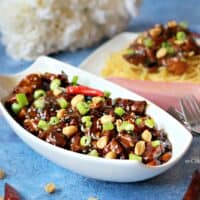 Kung Pao Chicken in a white serving dish topped with peanuts and red chili