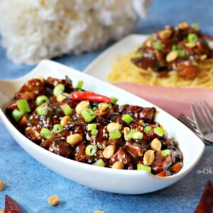 Kung Pao Chicken in a white serving dish topped with peanuts and red chili