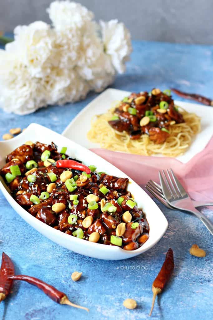 Kung Pao Chicken in a white serving dish with a plate of noodles behind it