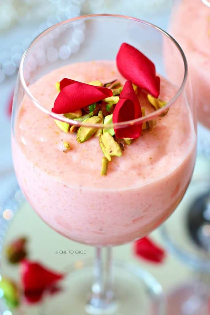 Firni in a stem glass topped with rose petals and chopped pistachio