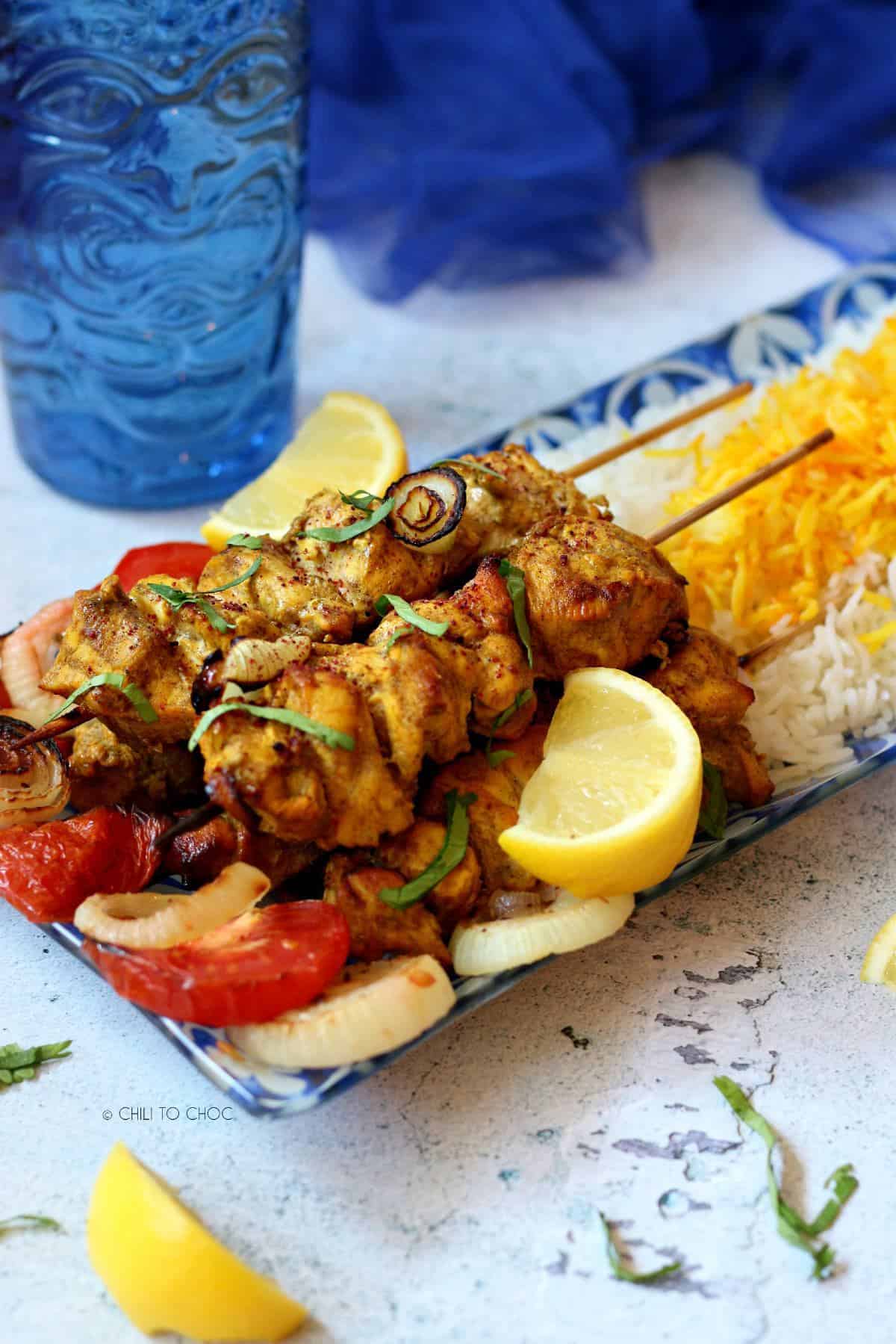 Persian chicken kabab skewers on a bed of grilled vegetables.