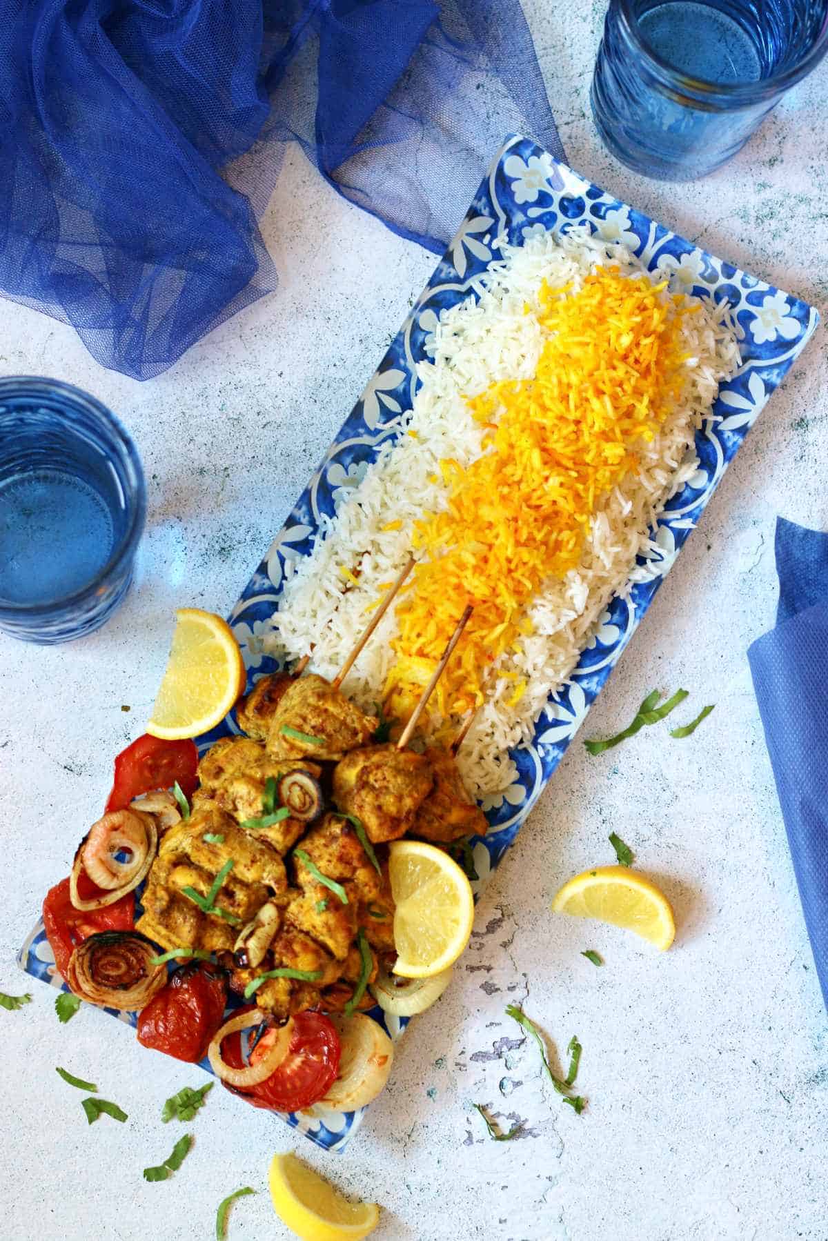 Overhead shot of joojeh kabob on saffron rice and lemon wedges.