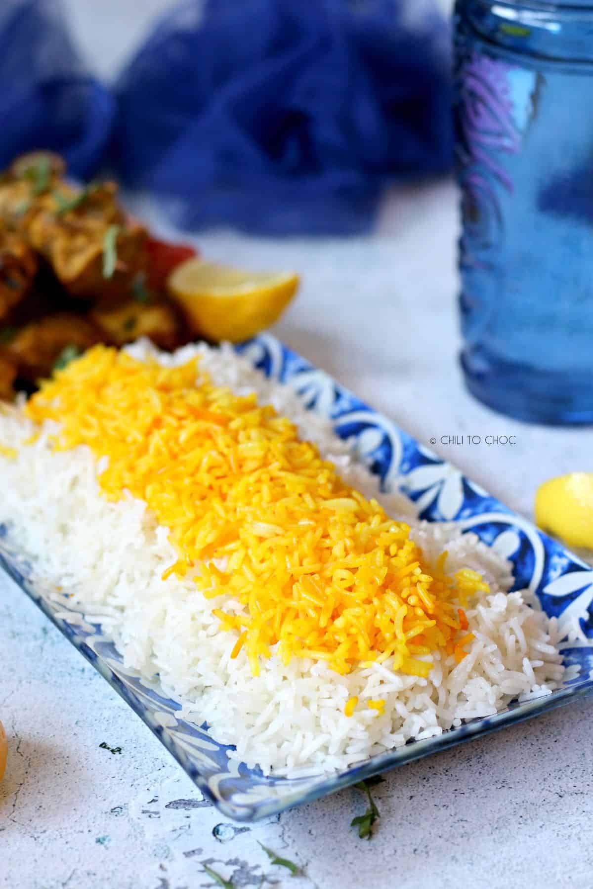 Plain basmatic rice topped with saffron rice on a blue dish.