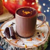 Orange hot chocolate in a transparent mug garnished with orange zest.