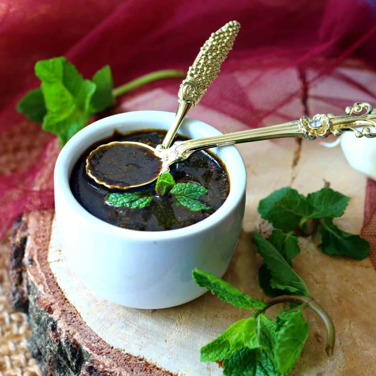 Green Tamarind Chutney in a white bowl with gold spoons inside