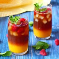 Two tall glasses of mango iced tea garnished with raspberries and mint