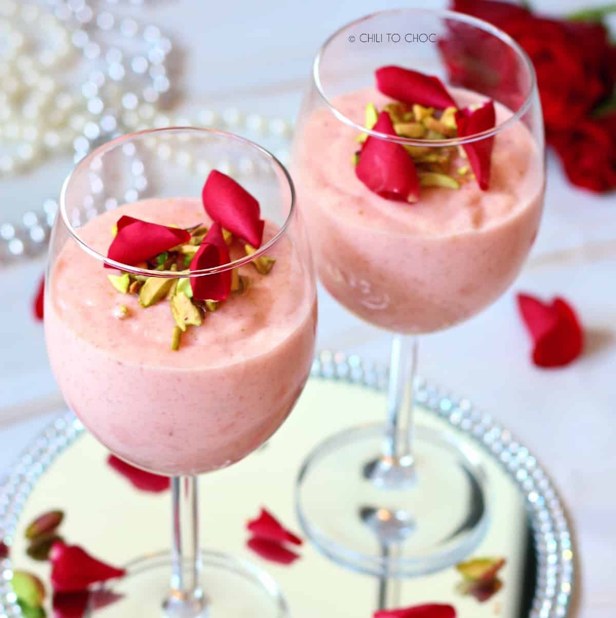 Rose and pistachio firni in 2 stem glasses garnished with rose petals.