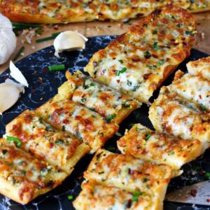 Slices of cheesy garlic bread served on a black platter with chives on top