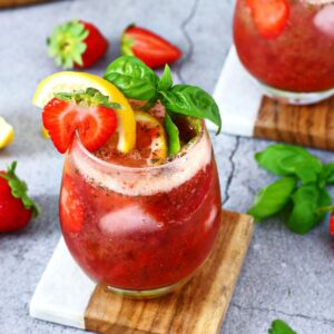 Strawberry Basil Lemonade in a glass with coaster underneath and garnished with lemon slice, basil leaf and half strawberry.