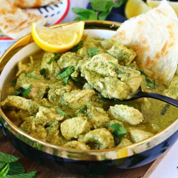 Hariyali (green) chicken in a dish with lemon wedges and paratha.