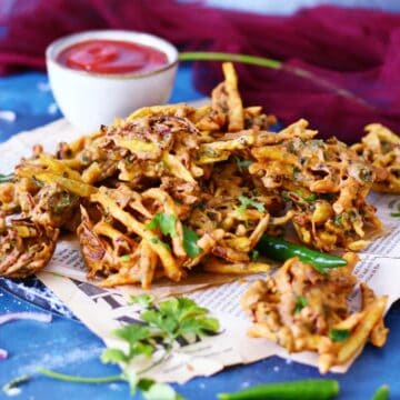 Vegetable pakoras on a newspaper with a ketchup bowl behind them.