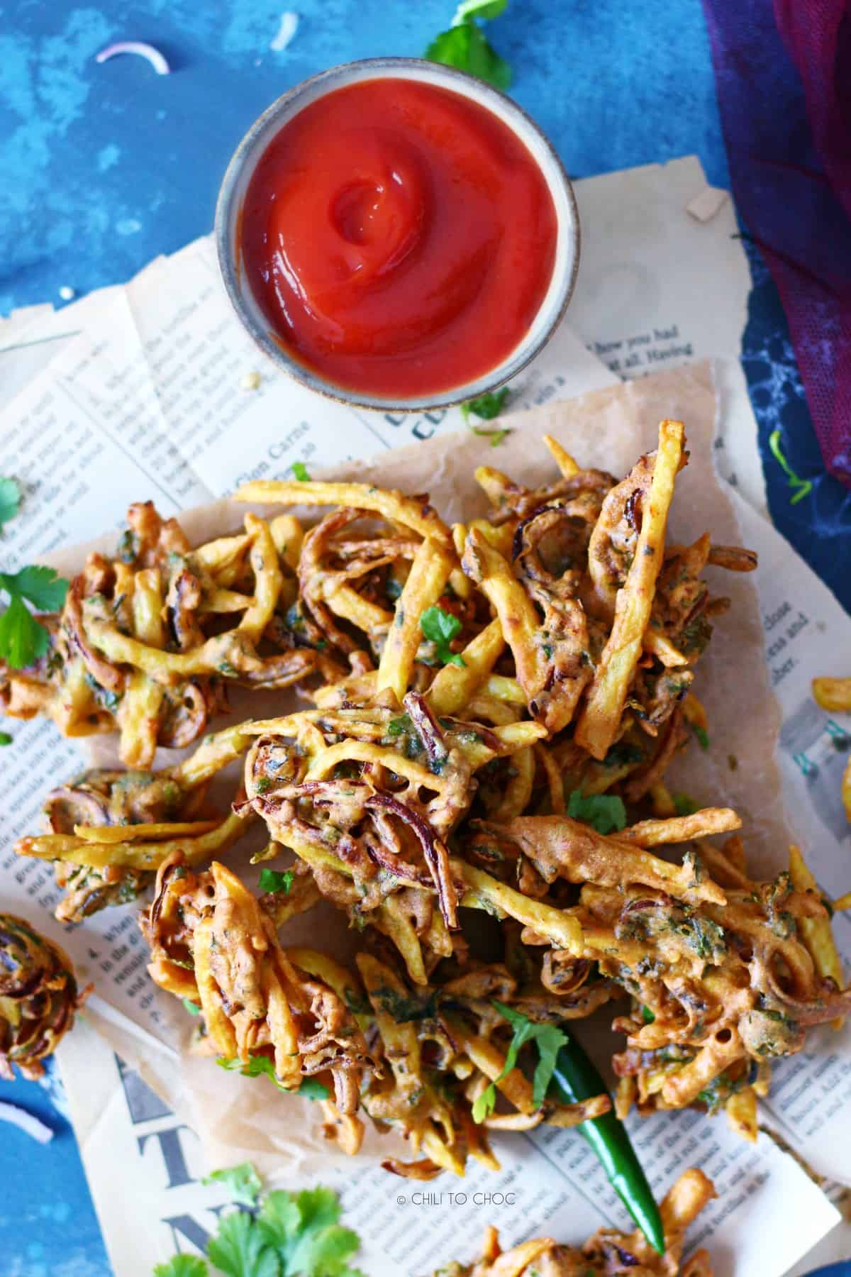 Pakoras randomly laid on a magazine paper with ketchup on the side.