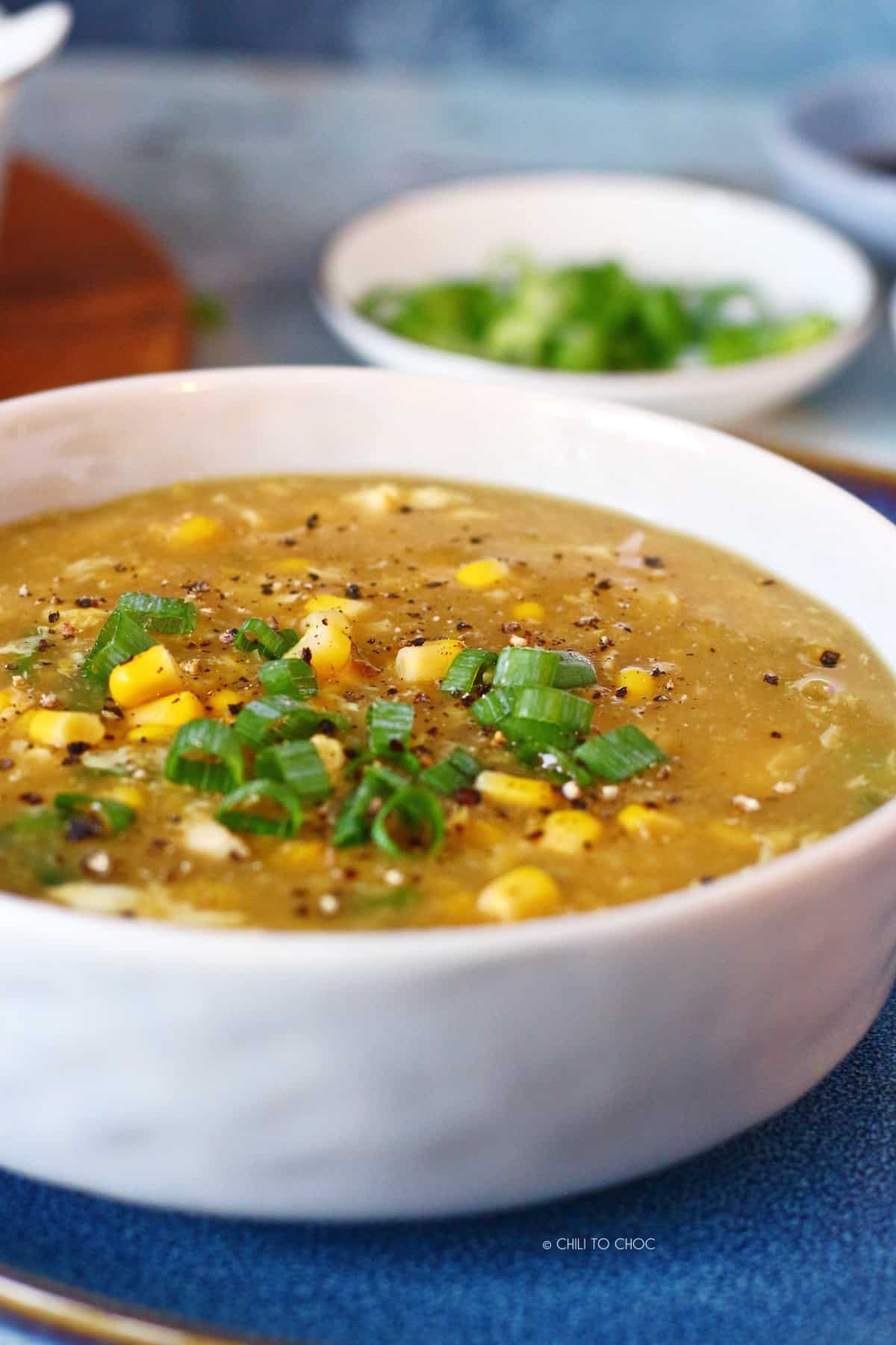 Chicken Corn Soup on a blue plate with sliced spring onion at the back.