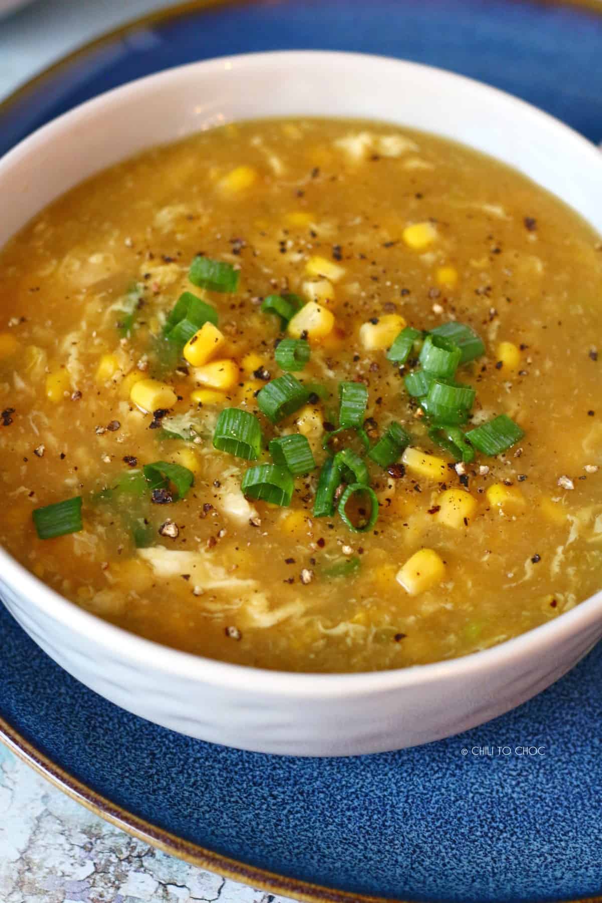 Close-up of chicken corn soup garnished with sweet corn kernels and spring onion.