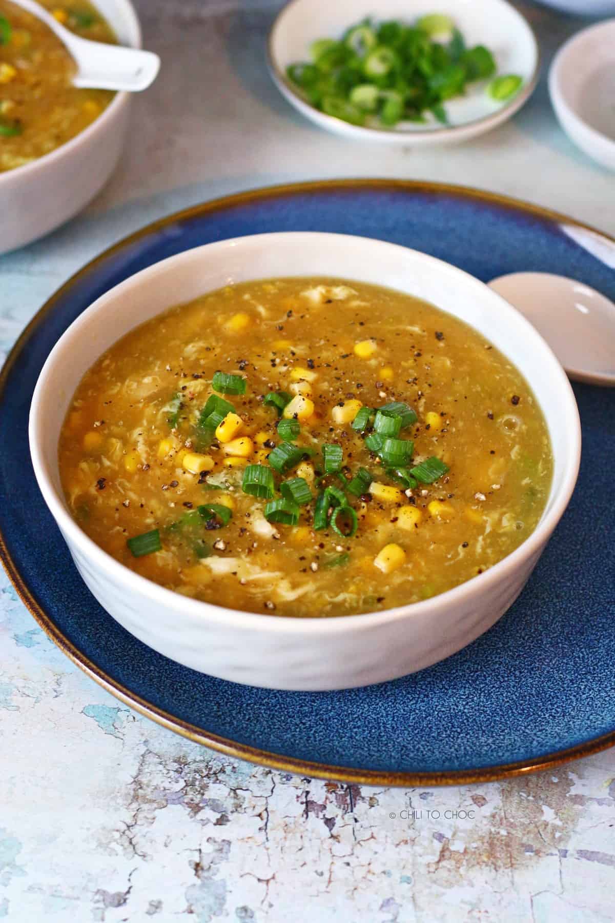 Bowl of chicken corn soup on a blue plate with a spoon on the side.