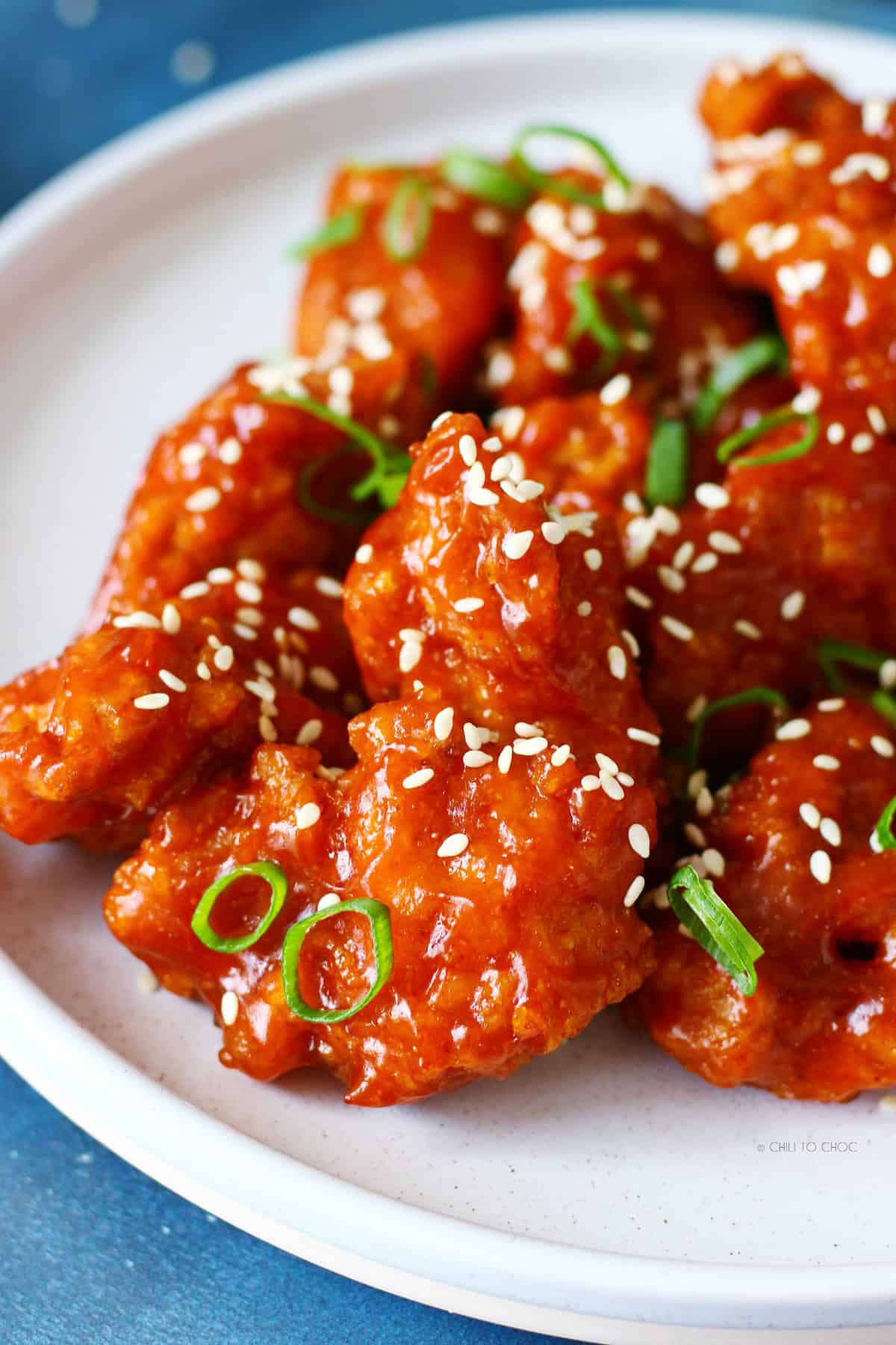 Closeup of honey sriracha chicken with a sticky glaze and white sesame seeds.