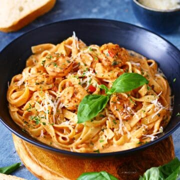 Creamy Cajun shrimp pasta in a black dish garnished with fresh basil, dried parsley and grated Parmesan.