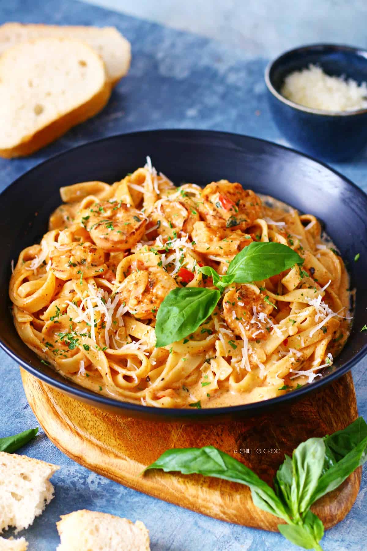 Creamy cajun shrimp pasta in a dish surrounded by sliced bread, fresh basil leaves and grated Parmesan cheese.