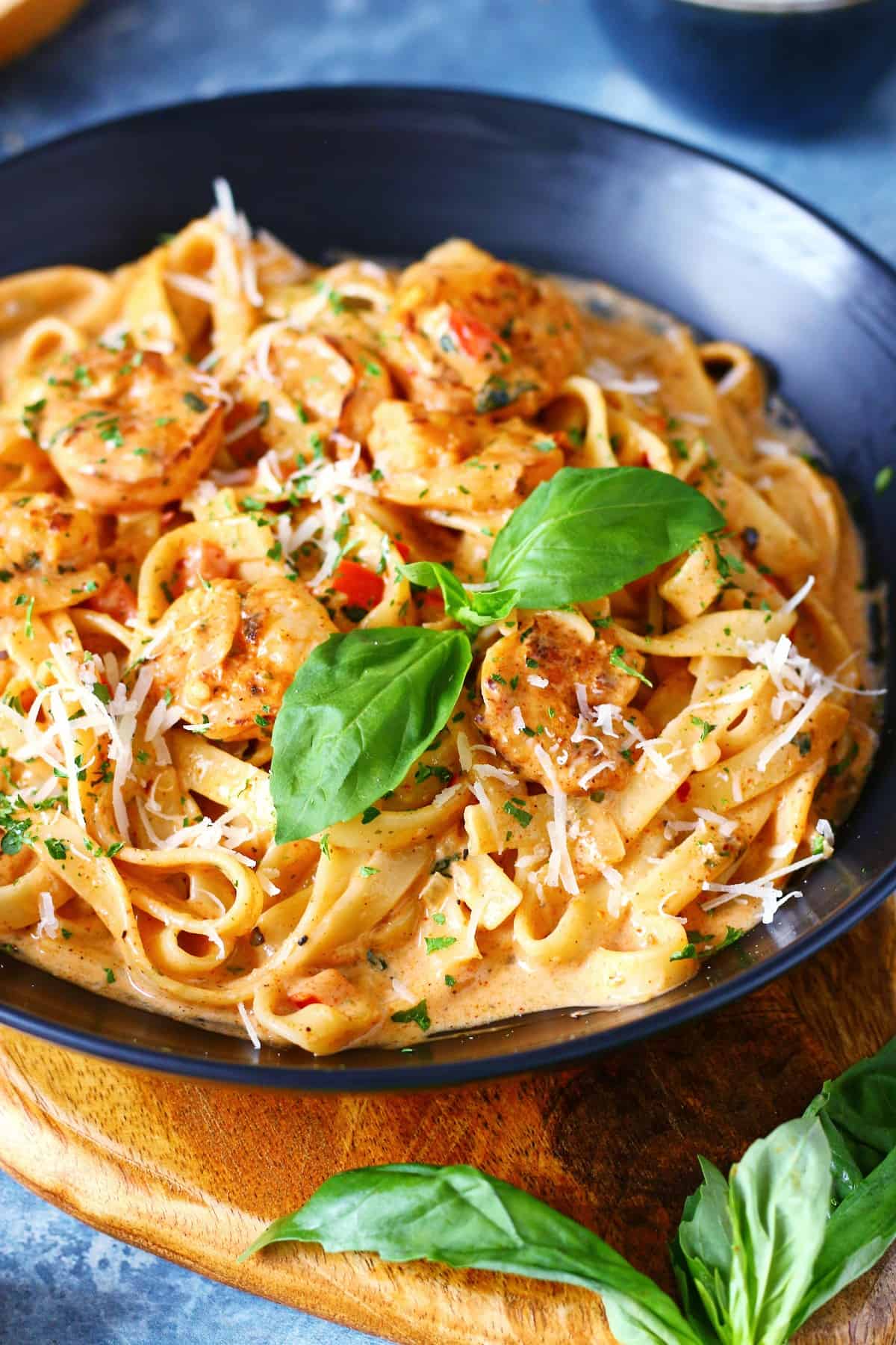 Creamy Cajun shrimp pasta with fresh basil leaf, grated Parmesan and dried parsley in a black dish.