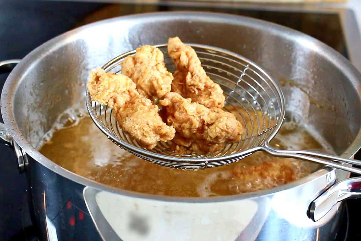 Taking out fried chicken from the pot in a slotted spoon.