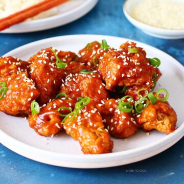 Honey sriracha chicken on a white plate garnished with green onion and sesame seeds.