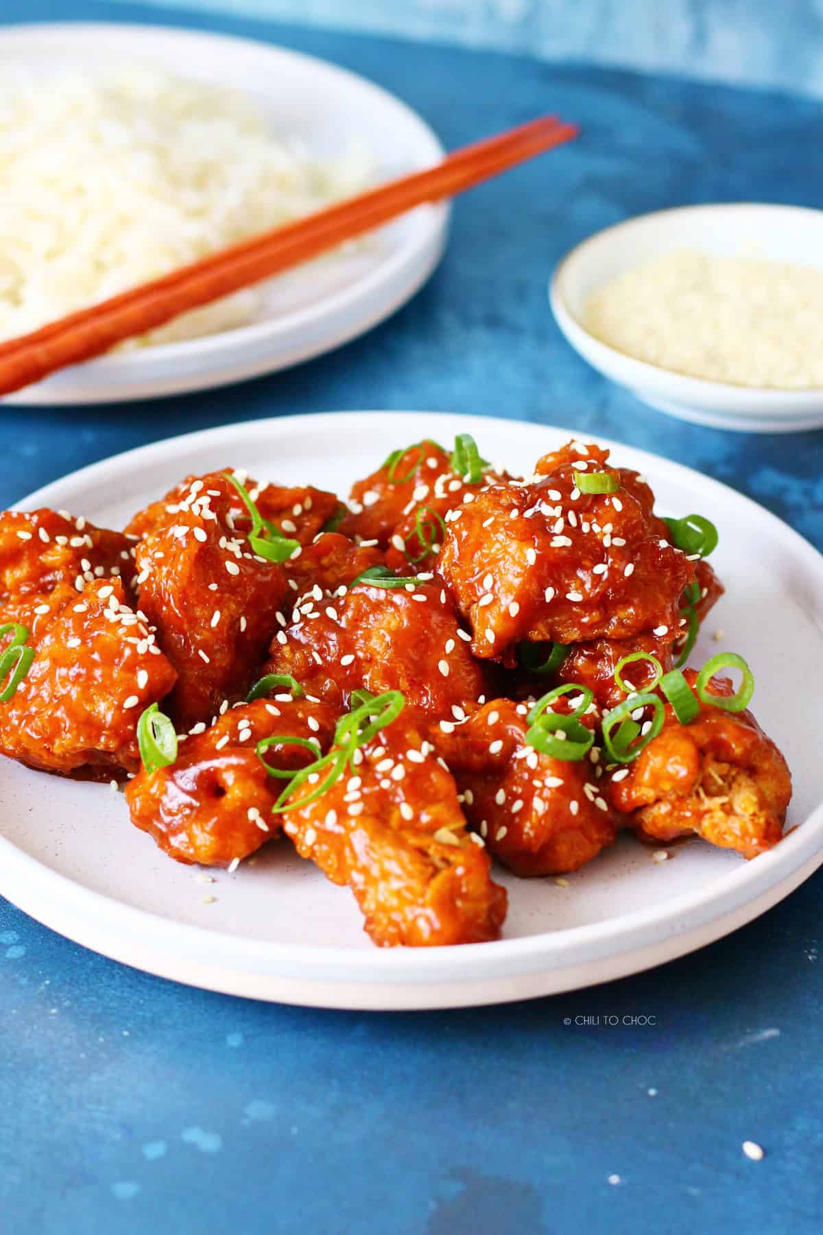 Honey sriracha chicken on a white plate with rice and sesame seed at the back.