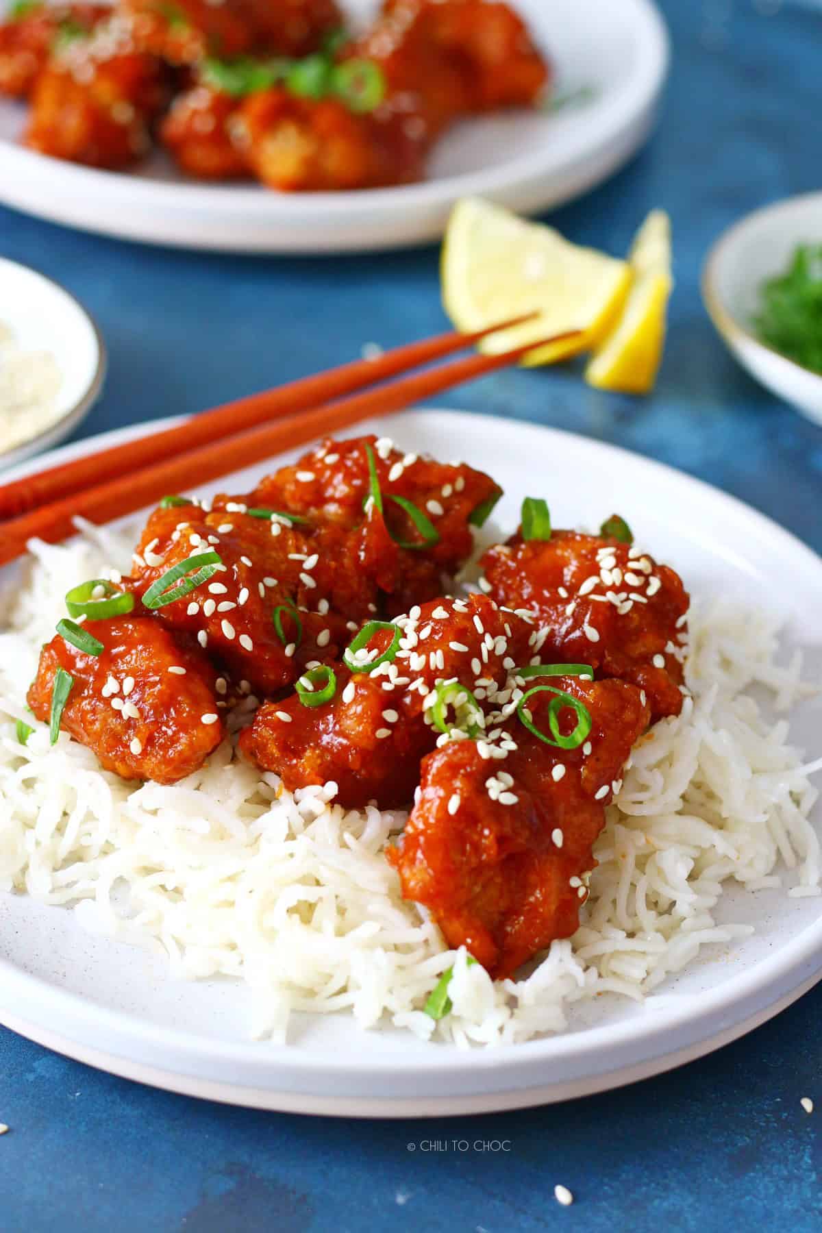 Crispy honey sriracha chicken on a bed of steamed white rice with chopsticks on the side.