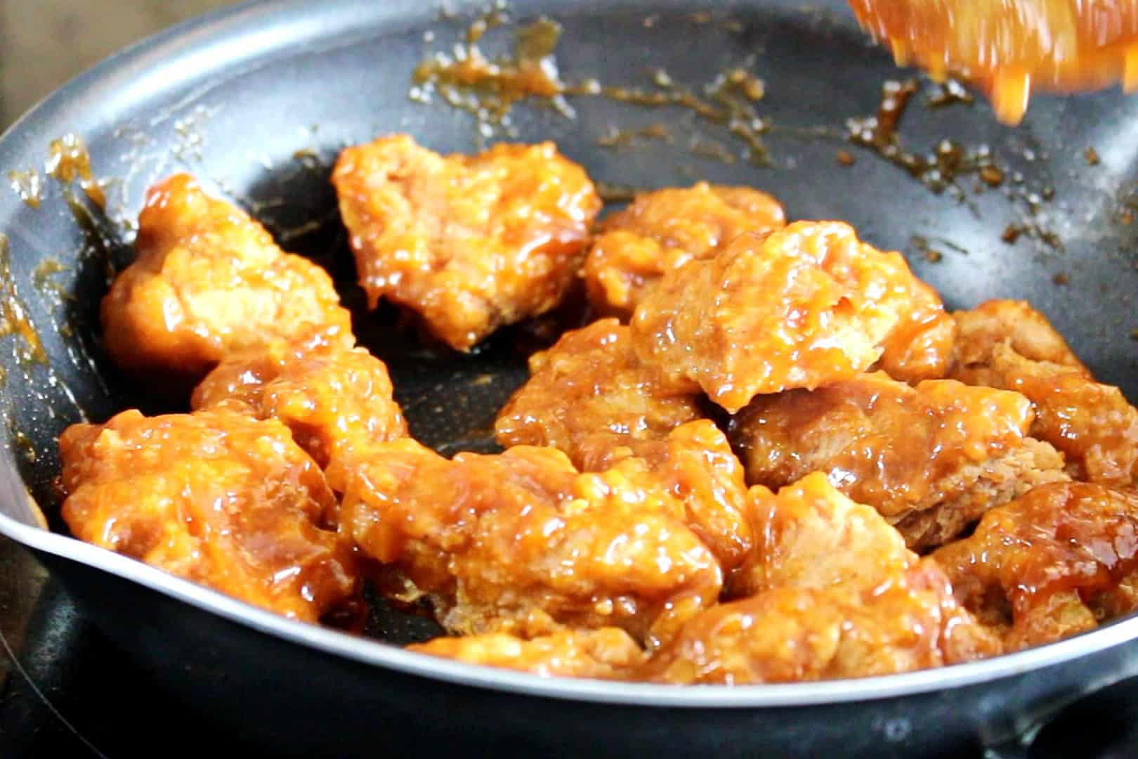 Chicken tossed with sticky sauce in a pan.