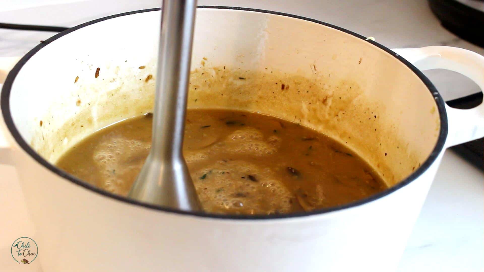 Using an immersion blender in a white dutch pot.