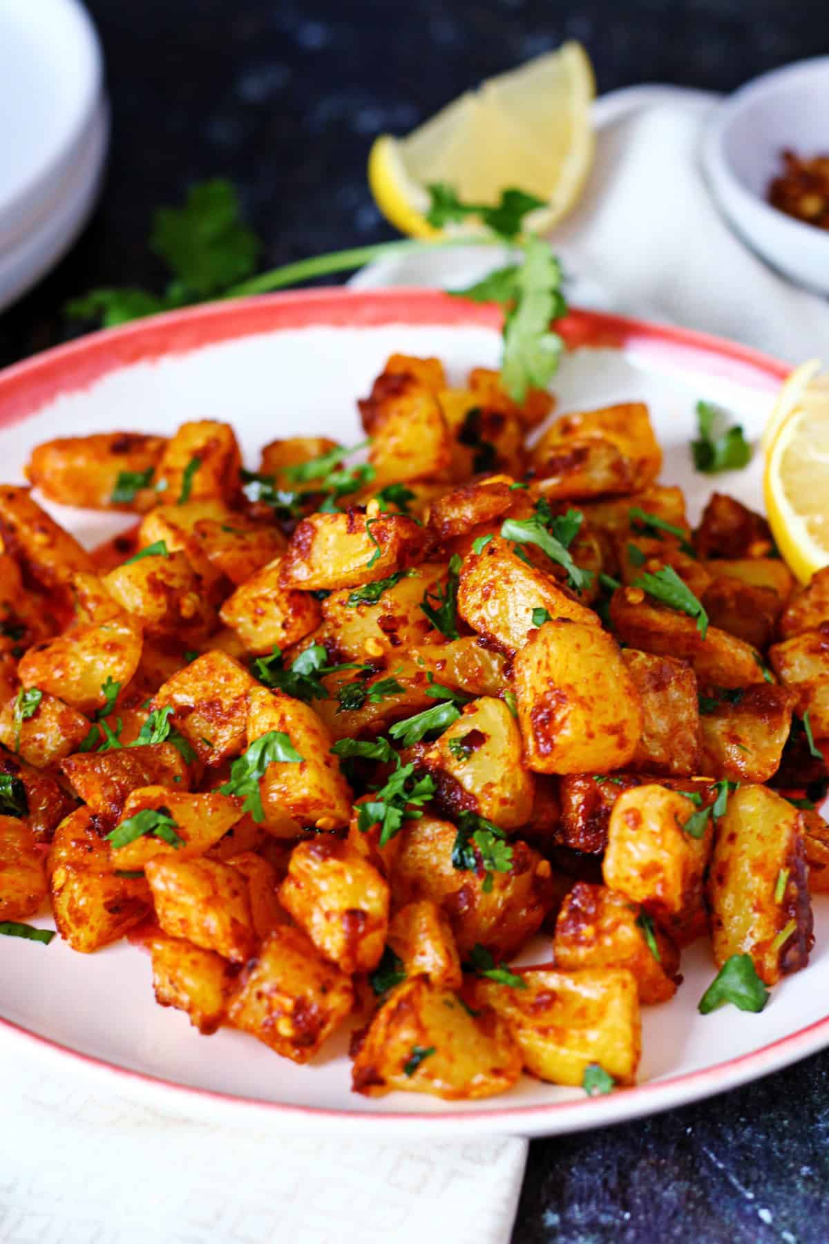 Batata Harra on a plate garnished with cilantro and a lemon wedge at the back.