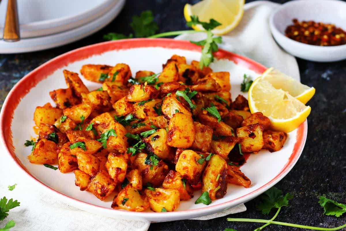 A plate of spicy Lebanese potatoes with lemon wedges and chopped cilantro as garnish and crushed red pepper at the back.