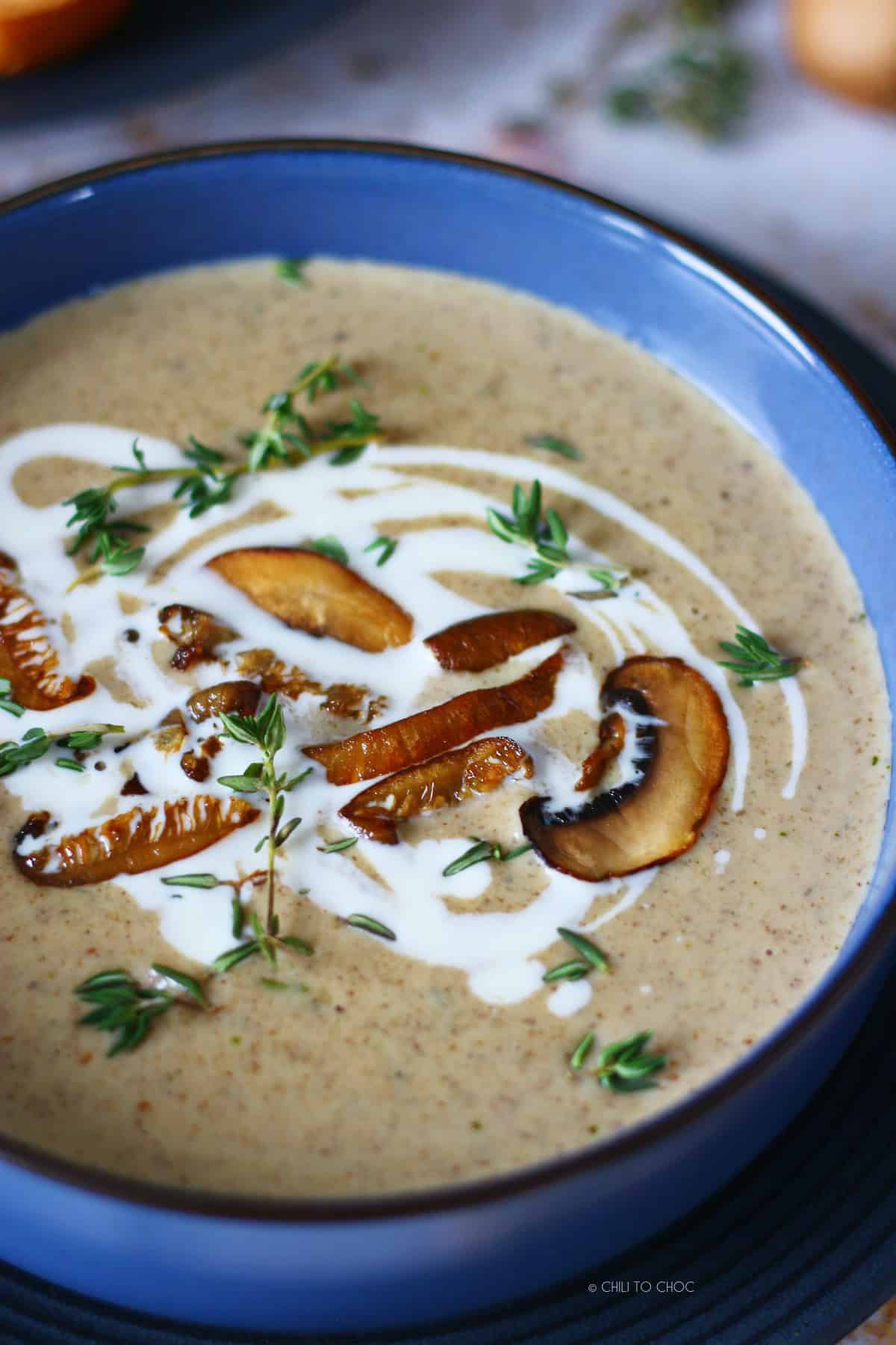 Close up of mushroom soup in a bowl garnished wit fresh thyme, sauteed mushrooms and cream.