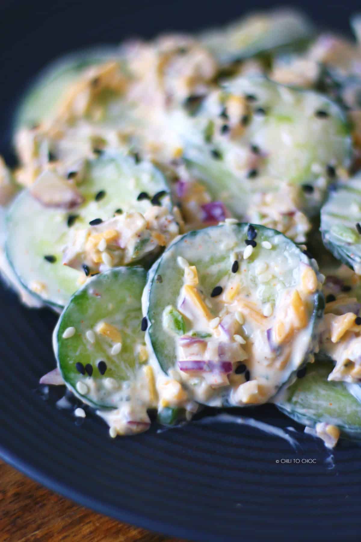 Closeup of cucumber salad with creamy cheese, sharp cheddar and sesame seeds.