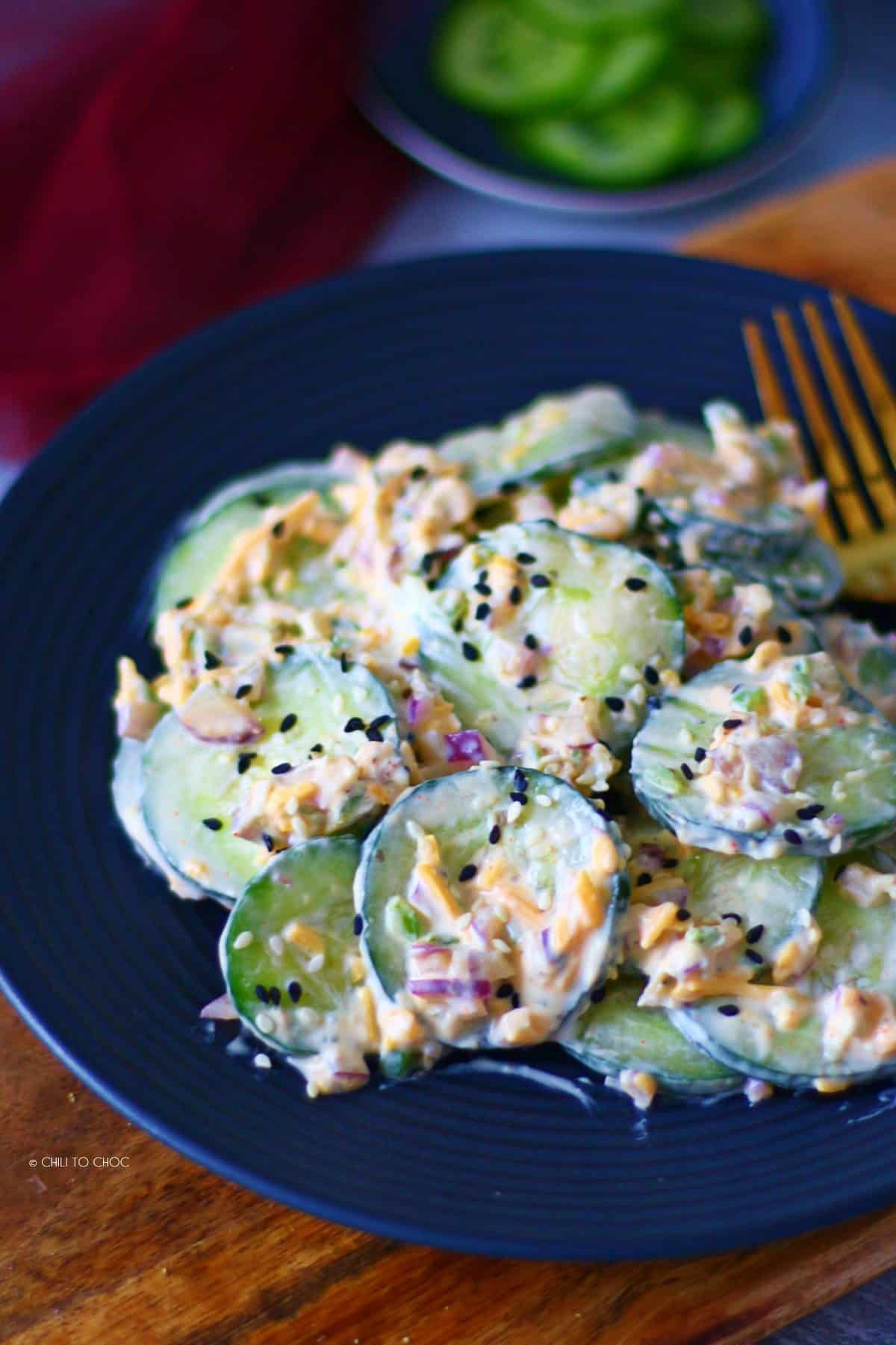 Jalapeno cucumber salad on a black plate with sliced cucumbers at the back.