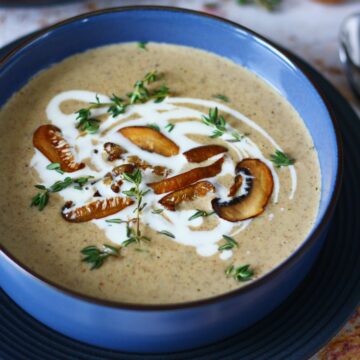 Mushroom Bisque in a blue bowl garnished with caramelized mushrooms, fresh thyme and cream.