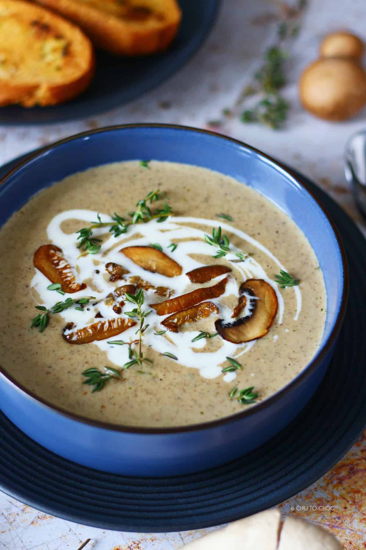 Mushroom soup in a blue bowl garnished with sauteed mushrooms, a swirl of cream and fresh thyme.