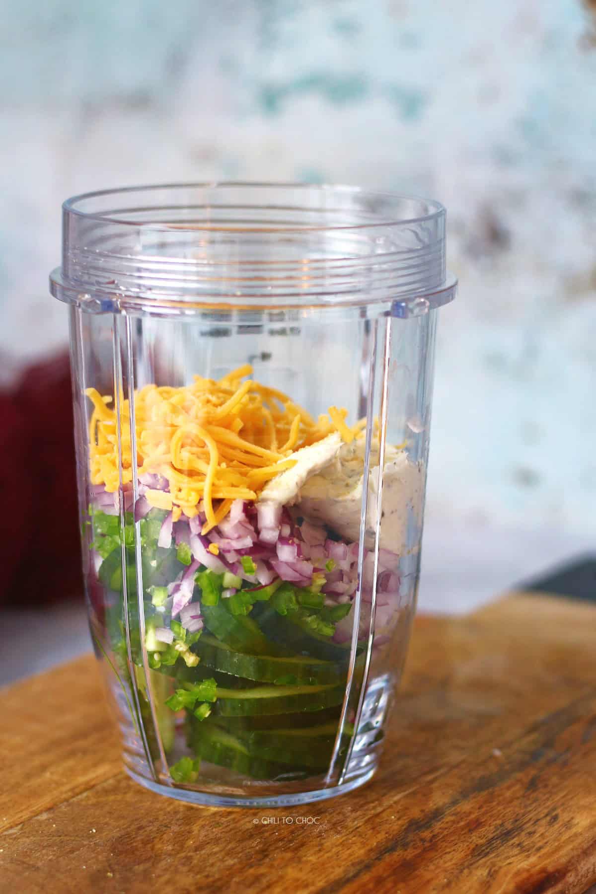 Layers of jalapeno popper cucumber salad ingredients in a jar.