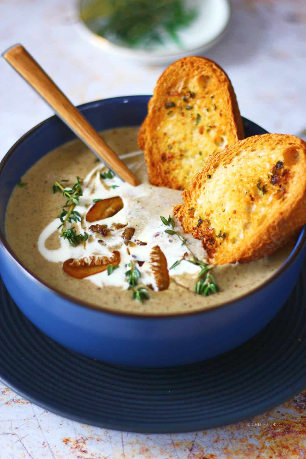 Two garlic breads dipped in a bowl of mushroom soup.