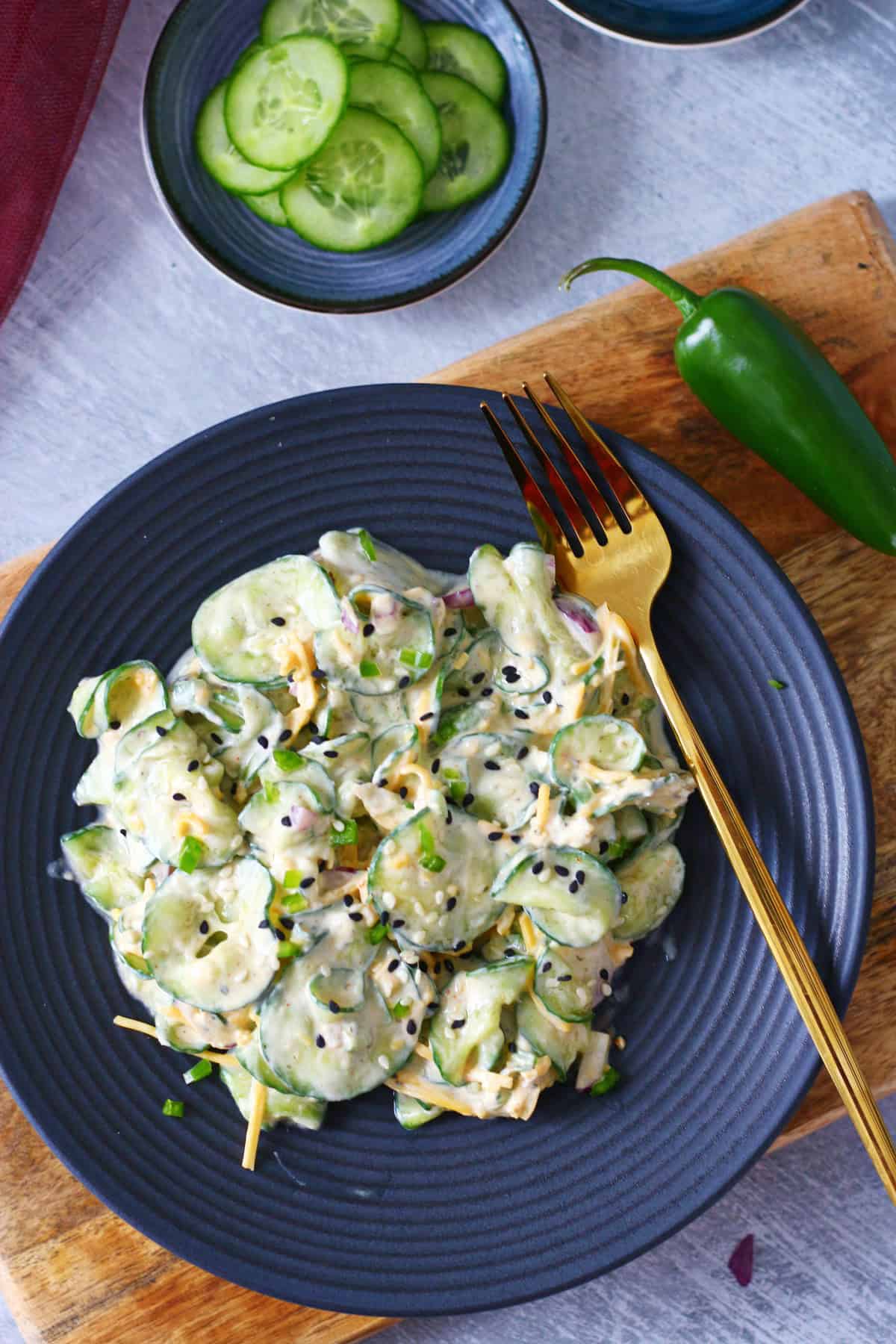 Top shot of thinly sliced cucumber salad in a black plate with gold fork on the side.