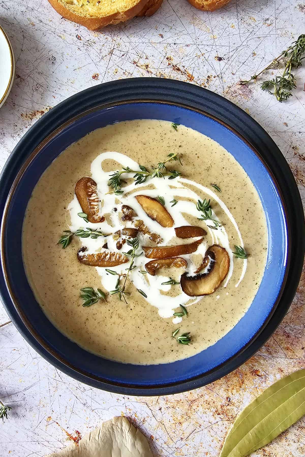 Mushroom soup garnished with crispy mushrooms, cream and fresh thyme surrounded by other ingredients.