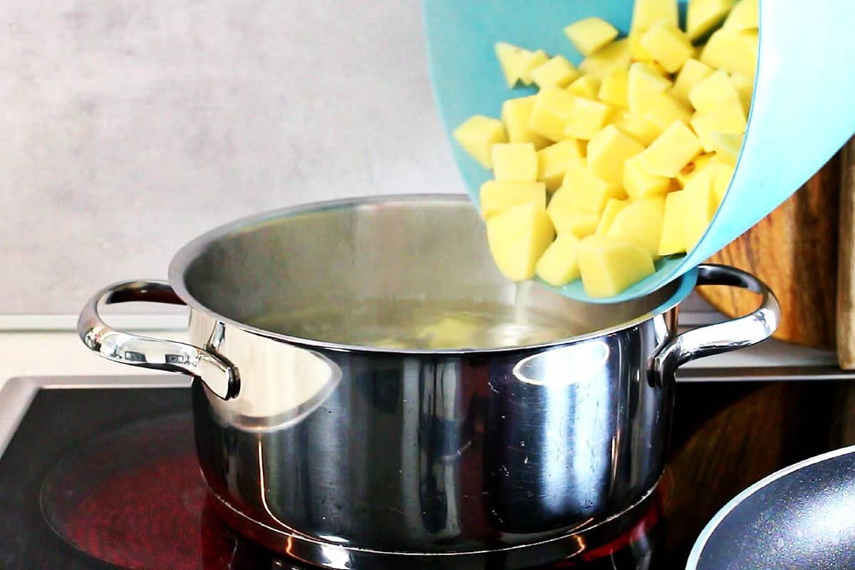 Adding cubed potatoes to a pot of boiling water.