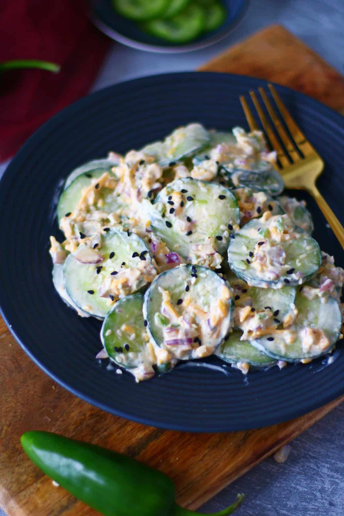 Cucumber salad on a black plate with gold fork on the side.