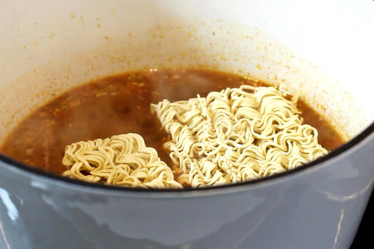 Uncooked egg noodles with soup broth in a Dutch pot.