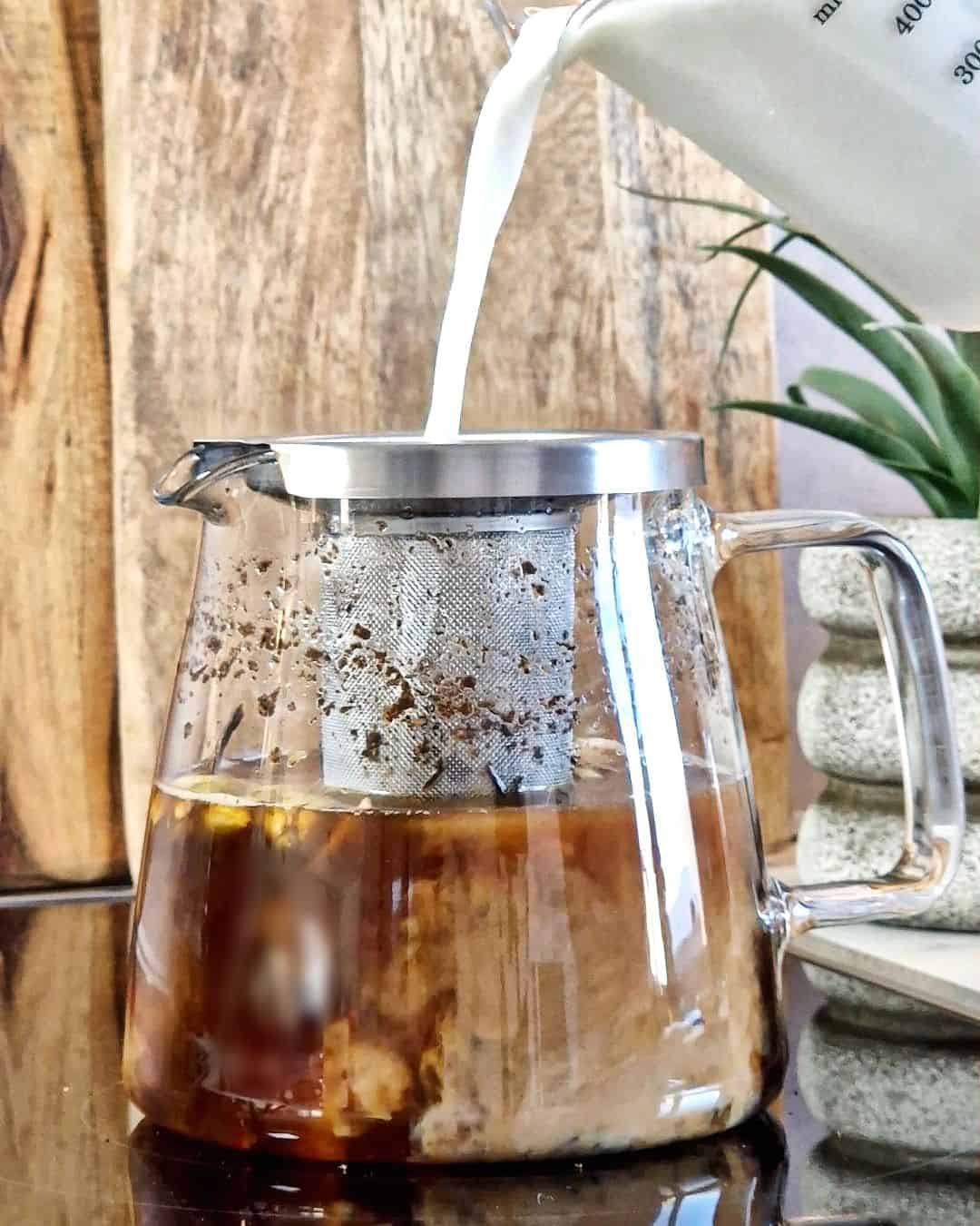 Adding milk to black tea in a glass kettle.