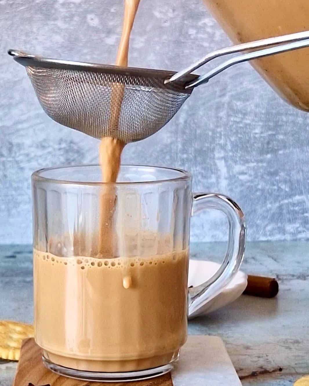 Straining milk tea into a clear mug.