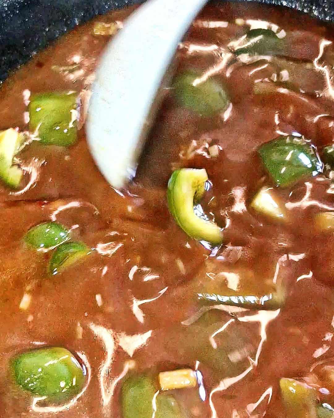 Sauce with bell peppers being stirred in a pan.